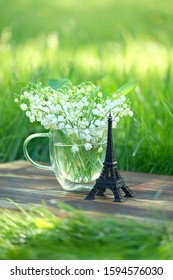 Eiffel Tower Decor And Lily Of The Valley Flowers In Glass Cup, Green Natural Background. Romantic Symbol Of Love, Paris, France. Spring Floral Season