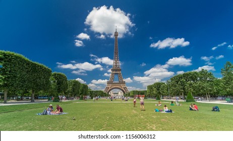 Eiffel Tower On Champs De Mars In Paris Timelapse Hyperlapse, France. Blue Cloudy Sky At Summer Day With Green Lawn And People Walking Around