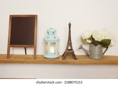 Eiffel tower statue, blue lantern, flower in metal vase and empty blackboard for copy on wooden shleves - Shutterstock ID 2188075213