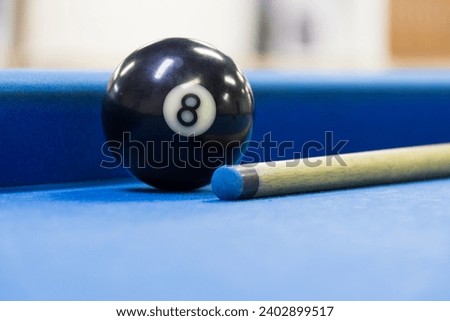 Eight ball next to a cue on the blue pool billiard table