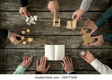 Eight businessmen planning a strategy in business advancement each holding  different but equally important metaphorical element - compass,  puzzle pieces, pegs, cubes, key and one making notes. - Shutterstock ID 334777604