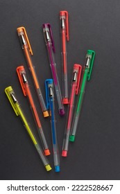 Eight Colorful Pens Scattered On Black Paper Surface, School And Office Stationery Concept, Taken From Above With Copy Space