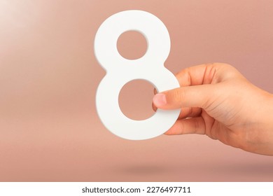 Eight in hand. A hand holds a white number 8 on a red background. Concept with number eight. Birthday 8 years, percentage, eighth grade or day, international women's day.