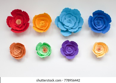 Acht handgemachte bunte Papierblumen in Regenbogenfarben auf weißem Hintergrund