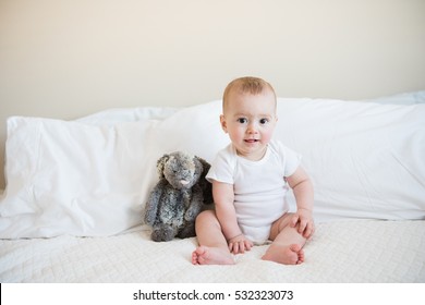 Eight Month Old Baby Boy In White Onesie Poses For Monthly Portrait