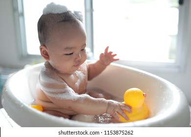 An eight months baby boy enjoying bathing time in his bath tub with floating yellow rubber duck.