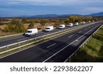 Eight white minivans are moving in a convoy on the highway. White delivery van on the highway. White modern delivery small shipment cargo courier van moving fast on motorway road to city urban suburb.