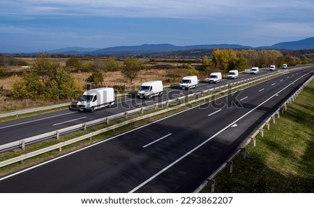 Eight white minivans are moving in a convoy on the highway. White delivery van on the highway. White modern delivery small shipment cargo courier van moving fast on motorway road to city urban suburb.