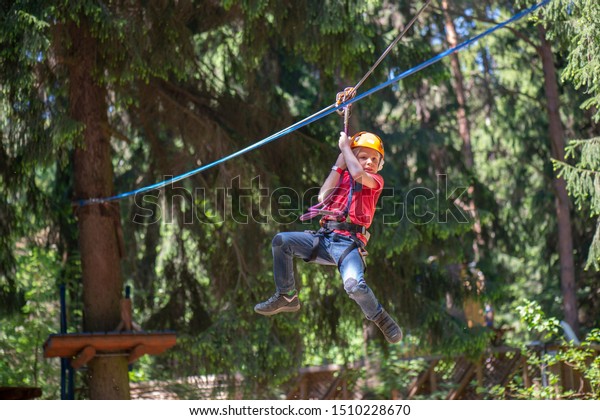 an eight-year-old\
boy slides along a horizontally pulled cable at high altitude while\
traversing a rope park