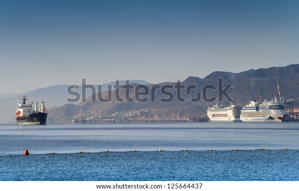EILAT, ISRAEL - JANUARY 22: Luxury AIDA and MSC\
ARMONIA cruise ships moored to marine port of Eilat on 22 January\
2013. Each ship is about 250 m long, has passenger capacity of 2000\
and 600-750 crew