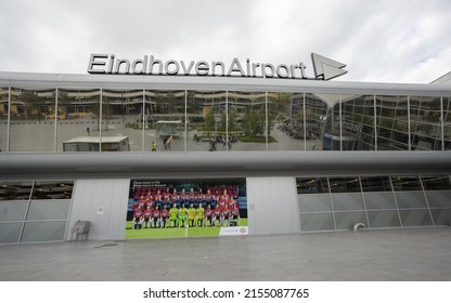 Eindhoven, Netherlands 5 May 2022 : Eindhoven Airport sign on top of terminal building and reflection of tourists walking and sitting in the glass window with photo of PSV Eindhoven football 