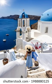 A ekegant woman in a blue dress walks down next to the popular blue domed church in the little village of Oia, Santorini, Greece, during summer travel time
