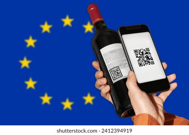 E-labeling of wine product in EU. Person scans QR code on label of wine bottle using mobile phone in front go flag of European Union. 
