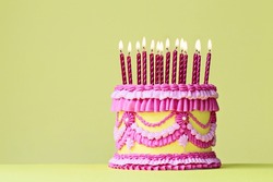 Elaborate Pink And Yellow Vintage Buttercream Birthday Cake With Birthday Candles And Piped Ruffles And Frills Against A Yellow Background