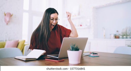 Elated excited successful female with long hair raising fist and screaming for celebrating victory watching on laptop at cozy apartment - Shutterstock ID 1577316841