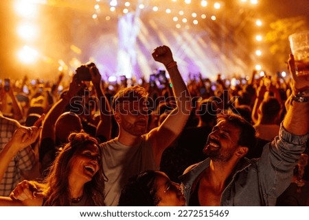 An elated group of young friends are excited to be at a concert, drinking and dancing in the night in front of the stage.