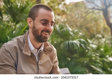 Elated Man Sitting On A Bench Outside And Smiling While Looking Downward