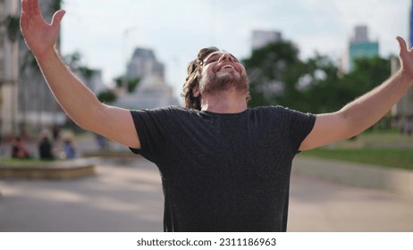 Elated young man gazing up at sky feeling the Grace of God. Believer feeling grateful and FAITH raises arms to sky feeling GRATITUDE - Shutterstock ID 2311186963