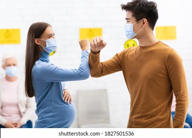 Elbow Bump Greeting. Pregnant Woman In Medical Mask Bumping Elbows Meeting A Friend Guy In Hospital Or Office Indoor. Social Distancing And Keeping Safe Distance For Covid-19 Protection Concept
