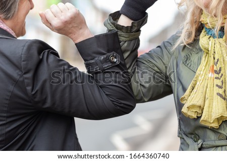 Elbow bump. New novel greeting to avoid the spread of coronavirus. Two women friends meet in a British street and instead of greeting with a hug or handshake, they bump elbows instead.