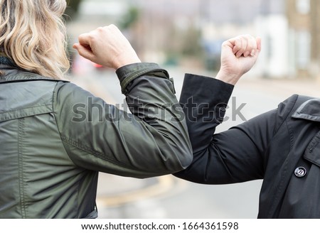 Elbow bump. New novel greeting to avoid the spread of coronavirus. Two women friends meet in a British street with bare hands. Instead of greeting with a hug or handshake, they bump elbows instead.