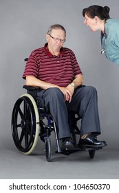 Elder Abuse Concept: Senior Man With Head Down In A Wheelchair As A Crazy Nurse Or Other Health Care Worker Is Yelling At Him