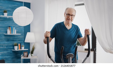 Elder adult doing physical cardio exercise on fitness bicycle. Aged man using electric stationary bike to do workout training at home. Old person with sport equipment to be in shape.