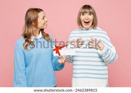 Elder amazed parent mom with young adult daughter two women together wear blue casual clothes hold gift certificate coupon voucher card for store isolated on plain pink background. Family day concept