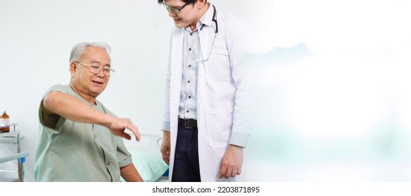 Elder Asian Man Sitting On The Bed And Talking To Doctor About His Physical Injuries At His Knees, Elderly Asian Man Having A Consulting With Professional Physical Therapist Or Orthopedic Doctor.