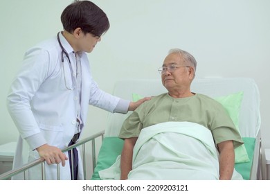 Elder Asian Man Sitting On The Bed And Talking To Doctor About His Physical Injuries At His Knees, Elderly Asian Man Having A Consulting With Professional Physical Therapist Or Orthopedic Doctor.