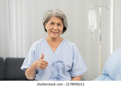 Elder Asian Woman Sitting On Bed With Receiving Saline Solution From Bag At Hospital Ward. Medicine, Health Care, Old People And Quarantine Concept