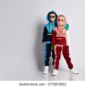 Elder bro hugging his younger sister. Stylish sporty kids in colourful tracksuits and sunglasses. Childhood, togetherness, friendship, loving siblings. Full length portrait isolated on light grey - Shutterstock ID 1772872052
