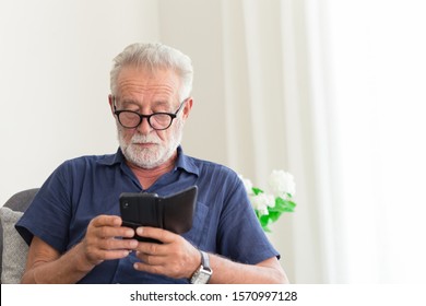 elder gray beard white hair with glasses looking attention at his smartphone to reading news at home alone.
