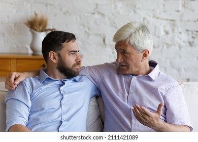 Elder grey haired loving father giving support and advice to grownup son. Senior parent and adult child talking on couch at home, discussing family life, keeping trusting relationships - Powered by Shutterstock