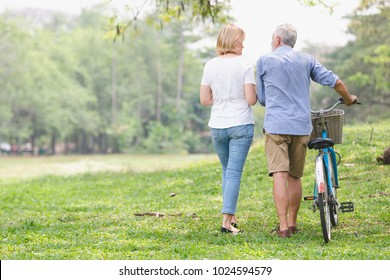 Elder Healthy Leisure Lifestyle,Senior Couple Walking Their Bike Along Happy Talking In The Park, Rear View Of An Older Caucasian Walk In A Park 