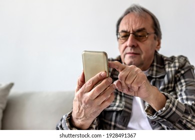 Elder Man Using A Mobile Phone While Relaxing At Home. Smiling Senior Man Wearing Eyeglasses Peer Down At His Smart Phone As He Tap Out A Text. Technology, People And Lifestyle Concept. Focus On Hands