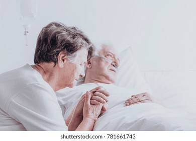 Elder Married Couple Sitting In The Hospital Holding Hands And Praying