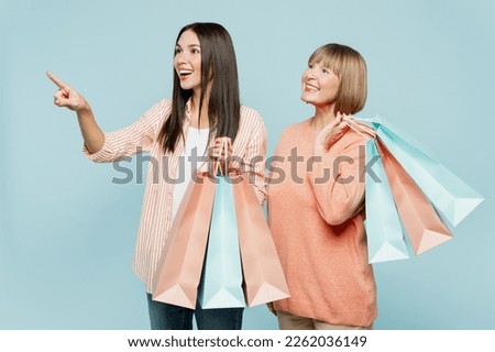 Elder mom with young adult daughter two women wear casual clothes hold paper package bags after shopping point aside ona area isolated on plain light blue background. Black Friday sale buy day concept Zdjęcia stock © 
