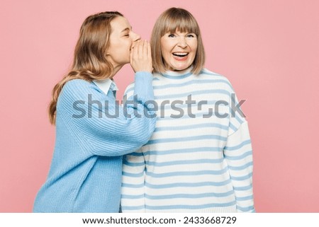 Elder parent mom 50s year old with young adult daughter two women together wear blue casual clothes whisper gossip and tell secret behind her hand isolated on plain pink background Family day concept