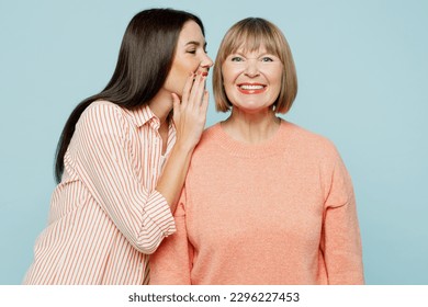 Elder parent mom with young adult daughter two women together wear casual clothes whispering gossip and tells secret behind her hand share news isolated on plain blue background. Family day concept - Powered by Shutterstock