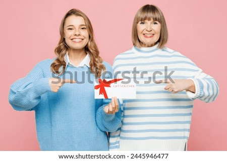 Elder parent mom with young adult daughter two women together wear blue casual clothes hold point on gift certificate coupon voucher card for store isolated on plain pink background Family day concept