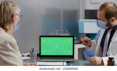 Elder Person Looking At Greenscreen On Laptop At Checkup Visit With Medic During Pandemic. Senior Patient And Doctor Analyzing Mockup Copyspace With Isolated Chromakey Template At Examination.