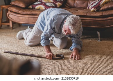 Elder senior man lying on floor after falling down with wooden walking stick beside couch on rug in living room at home. Old man suffering with pain and struggling to get up after falling down 