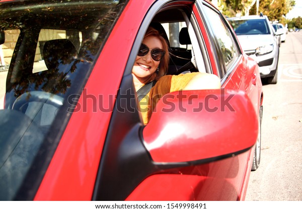 Elder style woman  sitting on red car and drive\
the vehicle