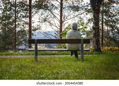 Elder woman sitting on bench at park during sunny day.