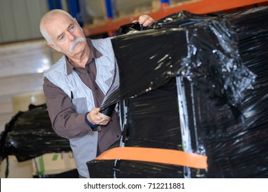 Elder Worker Using Shrink Wrap To Pack Items In Warehouse