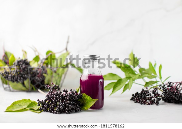 Elderberry syrup in a bottle, front\
view of ready to take-in syrup with raw ripe\
elderberries