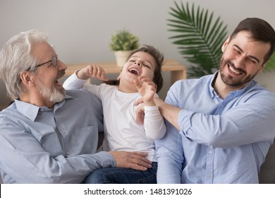 Elderly 60s Grandpa And Grown Up Son Tickling Small Adorable Boy, Cheerful Family Multi Generational Men Having Fun Laughing Feels Happy Sitting On Couch At Home, Leisure Activities Love Care Concept