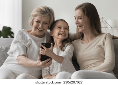 Elderly 60s granny her daughter and granddaughter laughing watch on-line videos sit on sofa using modern smart phone, feel carefree spend leisure on internet. Diverse generation using wireless tech - Powered by Shutterstock