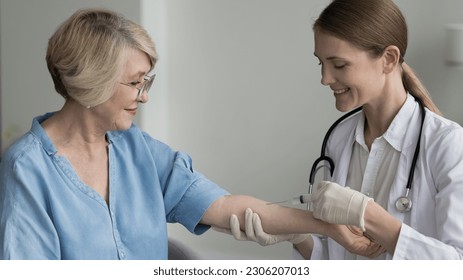 Elderly 60s woman receive professional medical care during visit in private clinic. Nurse in white coat hold syringe make injection to mature female hospital visitor. Diseases prevention, healthcare - Powered by Shutterstock